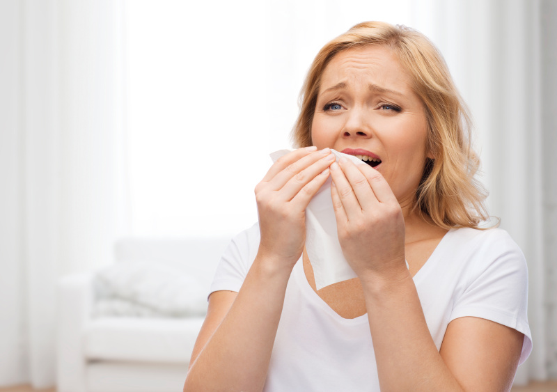 Eine Frau hält sich ein Taschentuch vor das Gesicht, weil sie niesen muss.