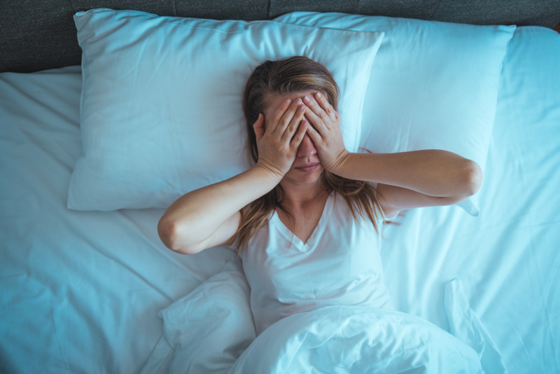 Eine junge Frau liegt im Bett und hält sich die Hände vor das Gesicht.