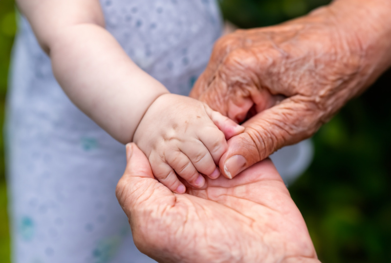Eine Kinderhand liegt in den Händen zweier alter Menschen.